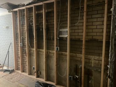 Exposed brick wall with wooden framing and electrical wiring during renovation.