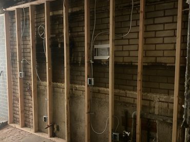 Exposed brick wall with wooden studs and electrical wiring during renovation.