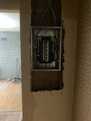 Exposed electrical panel with wiring inside a partially demolished wall.