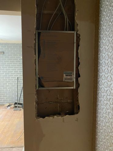 Wall cutout with exposed wiring and a cardboard box inside a framed opening.