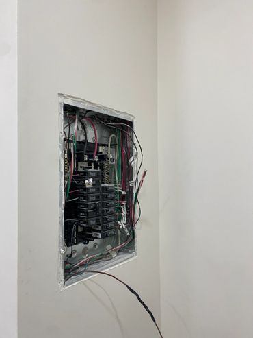 Open electrical panel with exposed wiring and circuit breakers.