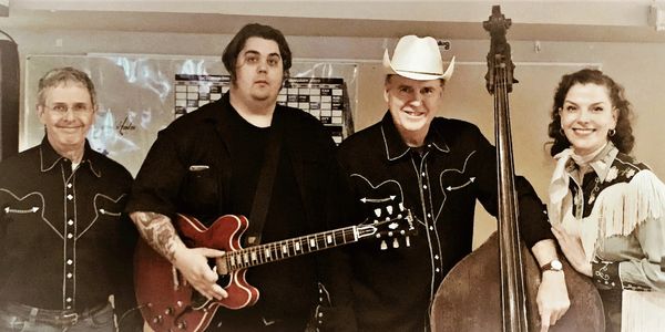 Four musicians posing with instruments and smiles.
