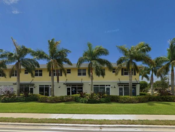 Yellow two-story building with palm trees and clear blue sky.