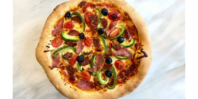 A freshly baked pizza with pepperoni, green peppers, olives, and tomatoes.