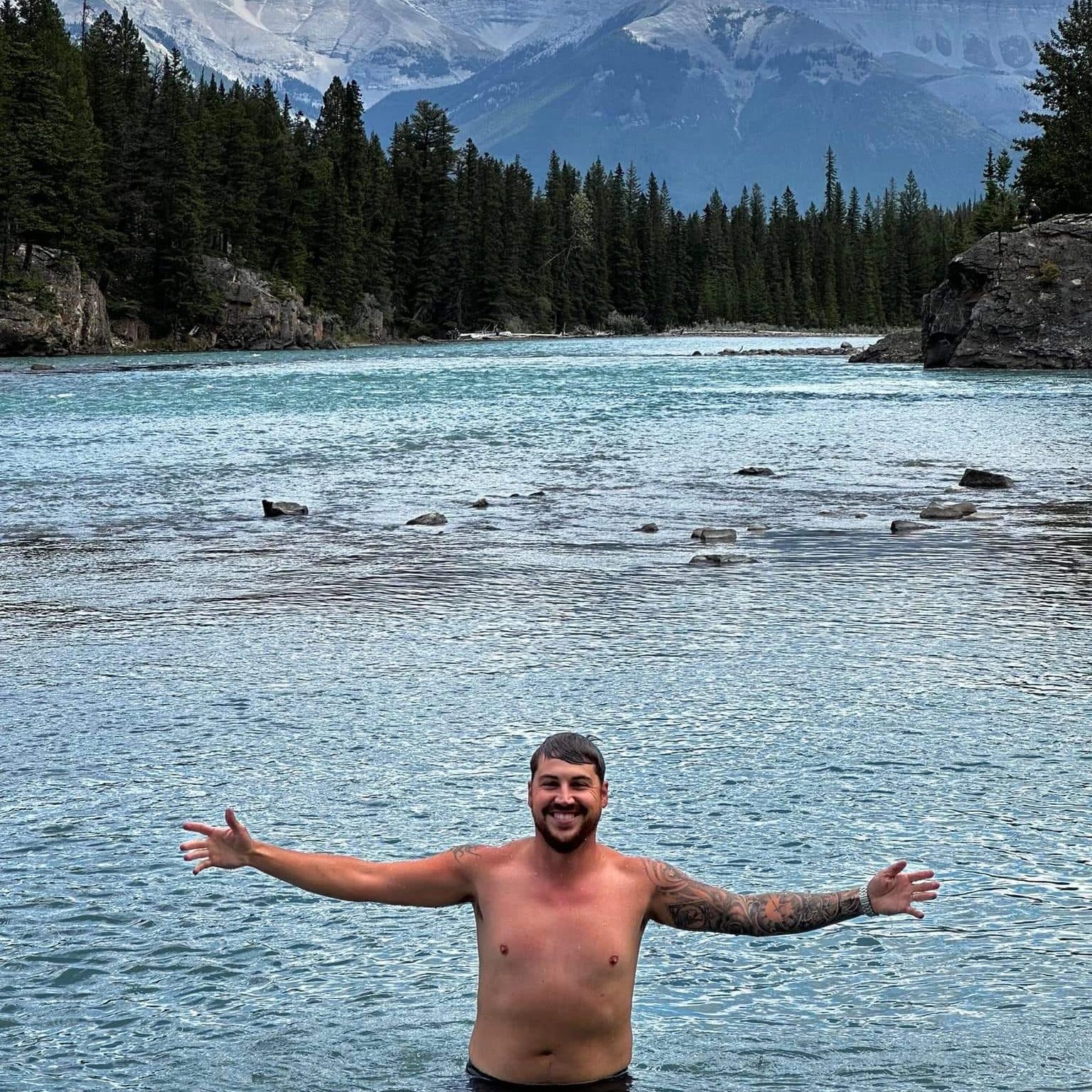 Happy man standing in cold mountain river with arms open wide.
