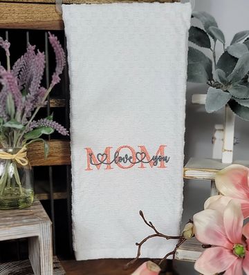 White towel embroidered with 'MOM I love you' surrounded by flowers.