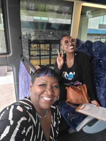 Two women smiling on a bus, one flashing a peace sign.