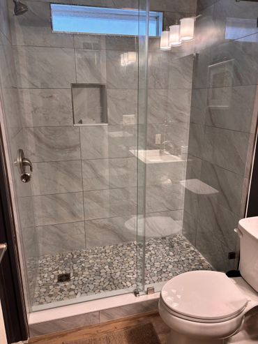 Modern bathroom shower with glass door and pebble floor tiles.