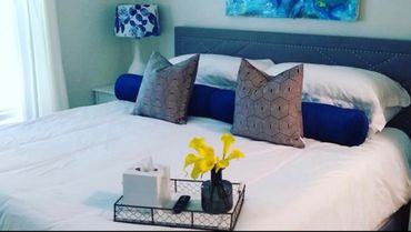 Modern bed with patterned pillows, blue bolster, and tray with flowers and tissues.