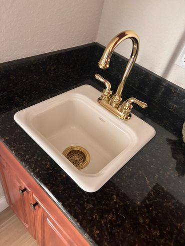 White sink with gold faucet and dark granite countertop.