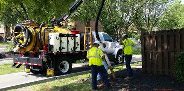 Workers operating a vacuum excavation truck in a residential area.
