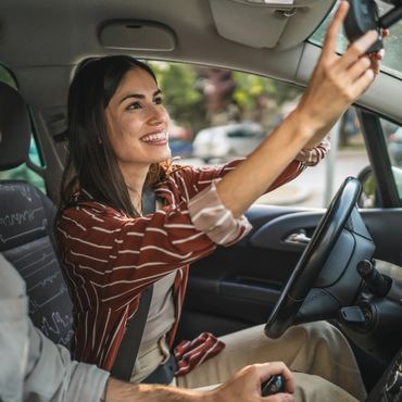 A woman smiling while adjusting the rearview mirror in a car.