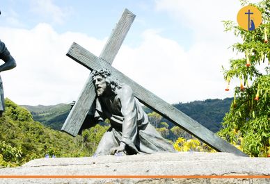 Escultura de Jesús cargando la cruz en un paisaje montañoso.