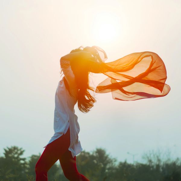 Une femme heureuse dans la nature avec un voile rouge et le soleil en arrière-plan