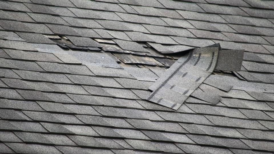A roof with wind damaged shingles possibly caused by slippage or improper installation.