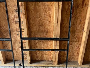 Black metal frame standing against wooden wall studs in a construction site.
