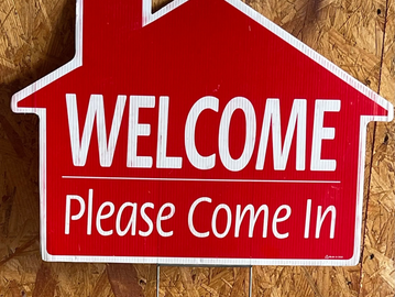 Red welcome sign shaped like a house saying 'Please Come In'.