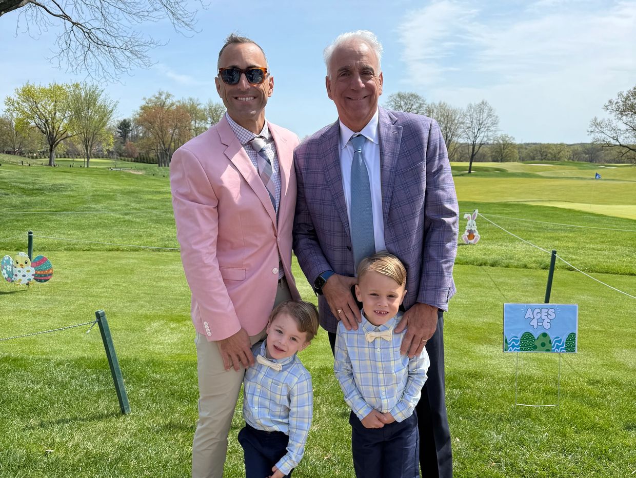 Two men and two boys posing on a grassy field on a sunny day.