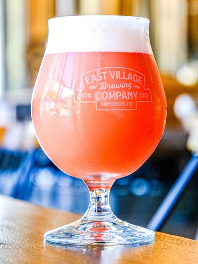 A glass of pink beer from East Village Brewing Company with a frothy head.