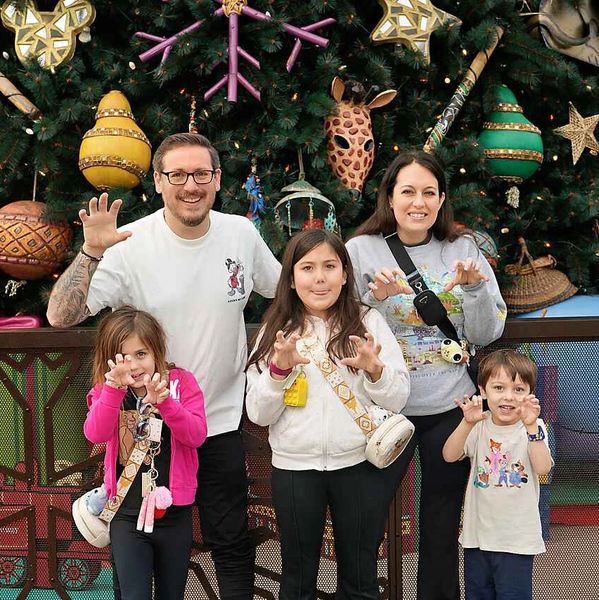 Family posing with playful claw hands in front of a decorated Christmas tree.