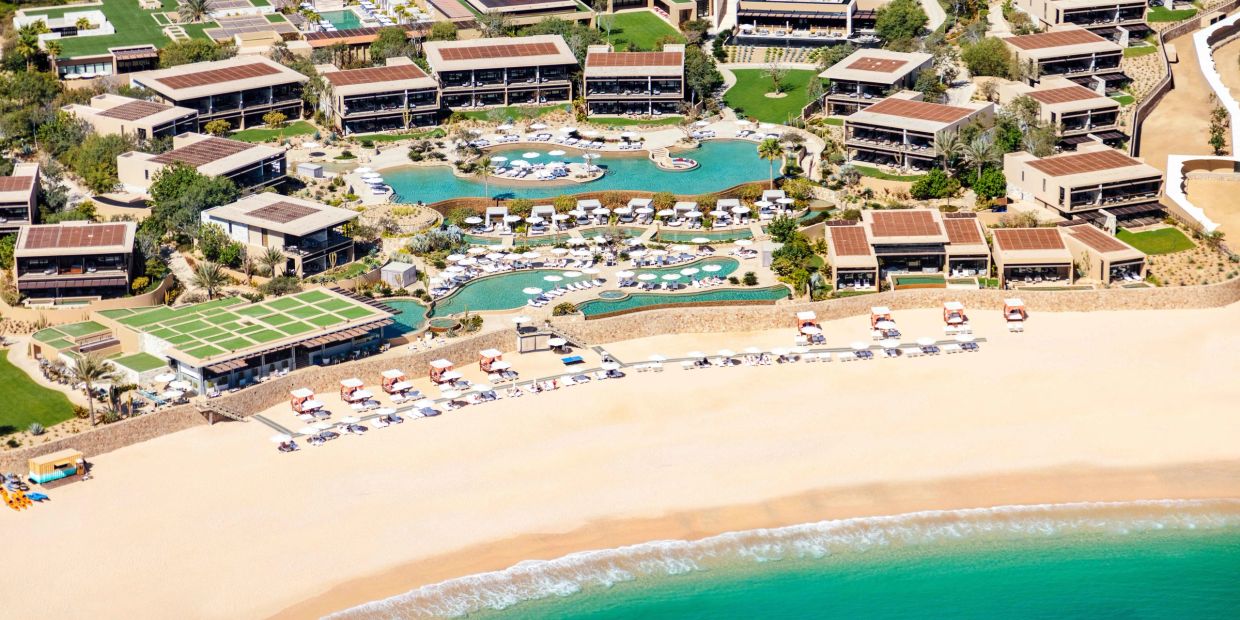 Aerial view of a beachfront resort with pools and sun loungers.