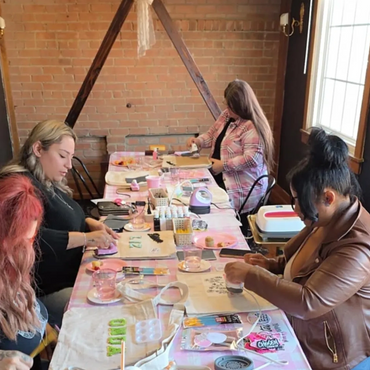 Women crafting at a table with various art supplies in a cozy room.