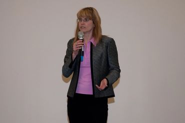 a woman standing in front of a white wall holding a microphone