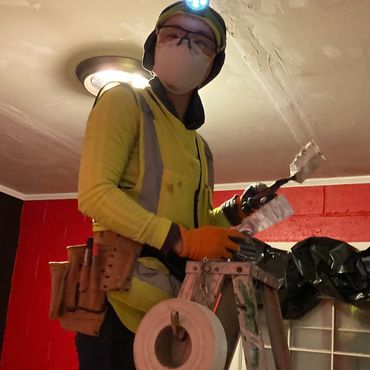 A woman on a ladder applying seam tape to the ceiling.
