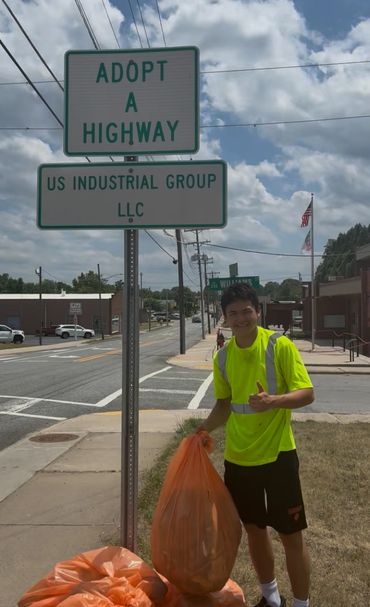Young man smiling at an Adopt-a-Highway sign.