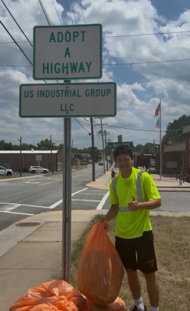 Young man holding trash bag under Adopt A Highway sign.