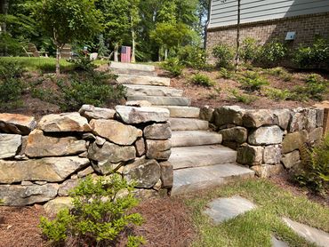 Natural stone steps and boulder retaining wall in a front yard landscape project in Dacula, GA