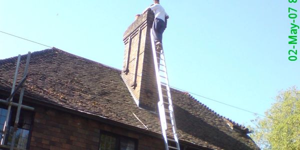 Person climbing a tall ladder to a chimney on a roof.