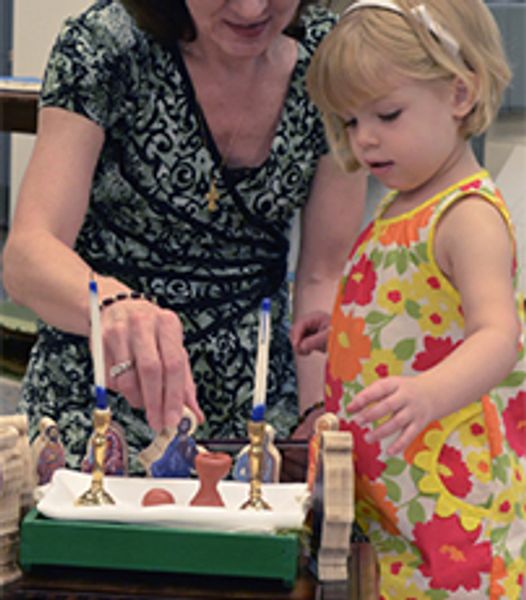 A woman and a child interact with a miniature nativity scene with candles.