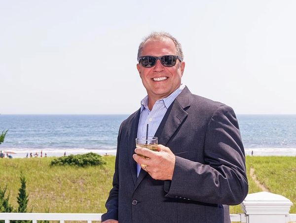 Peter smiling by the ocean holding a drink on a sunny day.