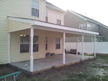 Newly constructed covered patio attached to a house with concrete flooring.