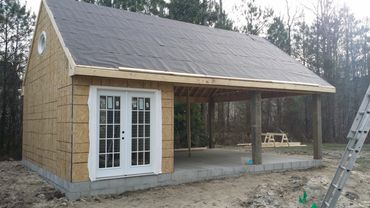 Partially constructed wooden building with white double doors and an open porch area.