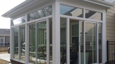 A modern sunroom with large glass windows and sliding door attached to a house.