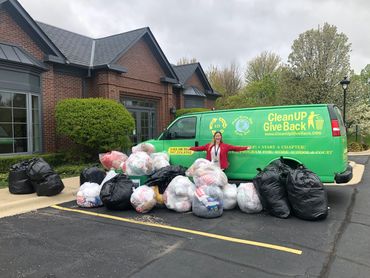 A lady in a red sweater posing in front of a large pile of plastic bags outside of a brick building