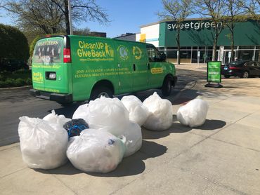 A large pile of Plastic Bags in front of Clean Up - Give Back's van, in front of sweetgreen building