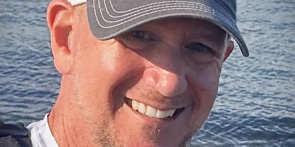 Smiling man wearing a cap near water.