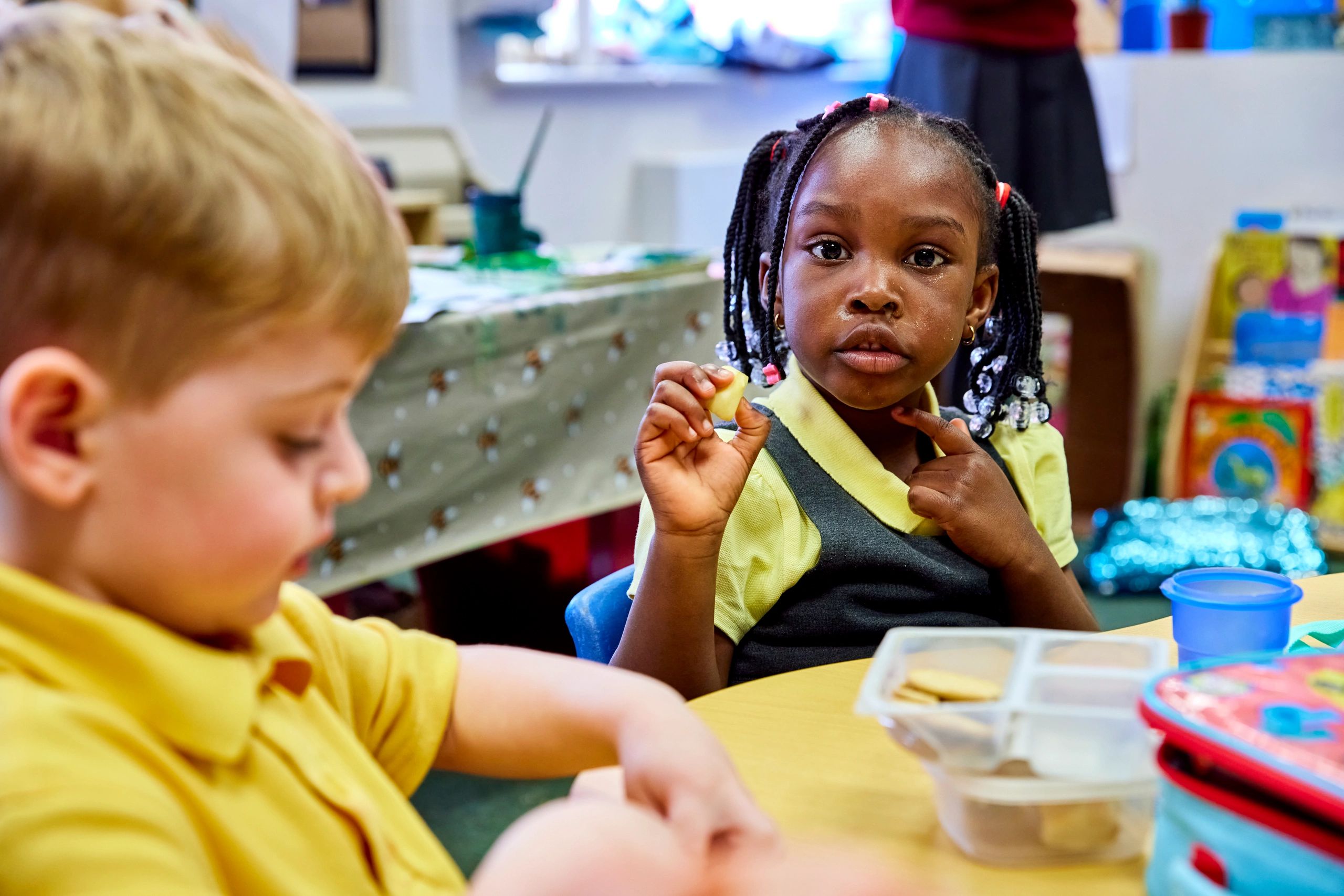 Two children sitting at a table, one holding a piece of food.