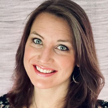 Smiling woman with blue eyes and brown hair posing against a textured background.