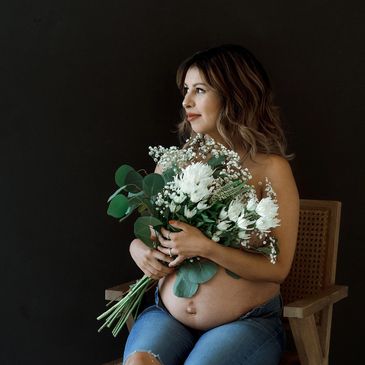 Pregnant woman sitting on chair holding a bouquet of white flowers.