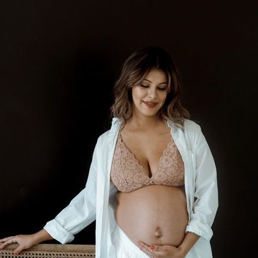 Pregnant woman gently holding her belly with a soft smile against a dark background.