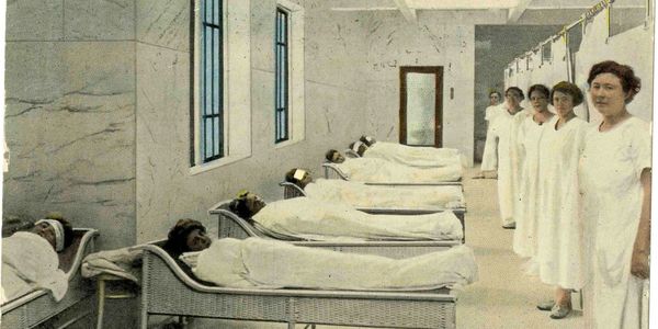 Vintage colorized photo of the ladies floor with patrons laying with hot packs and workers nearby