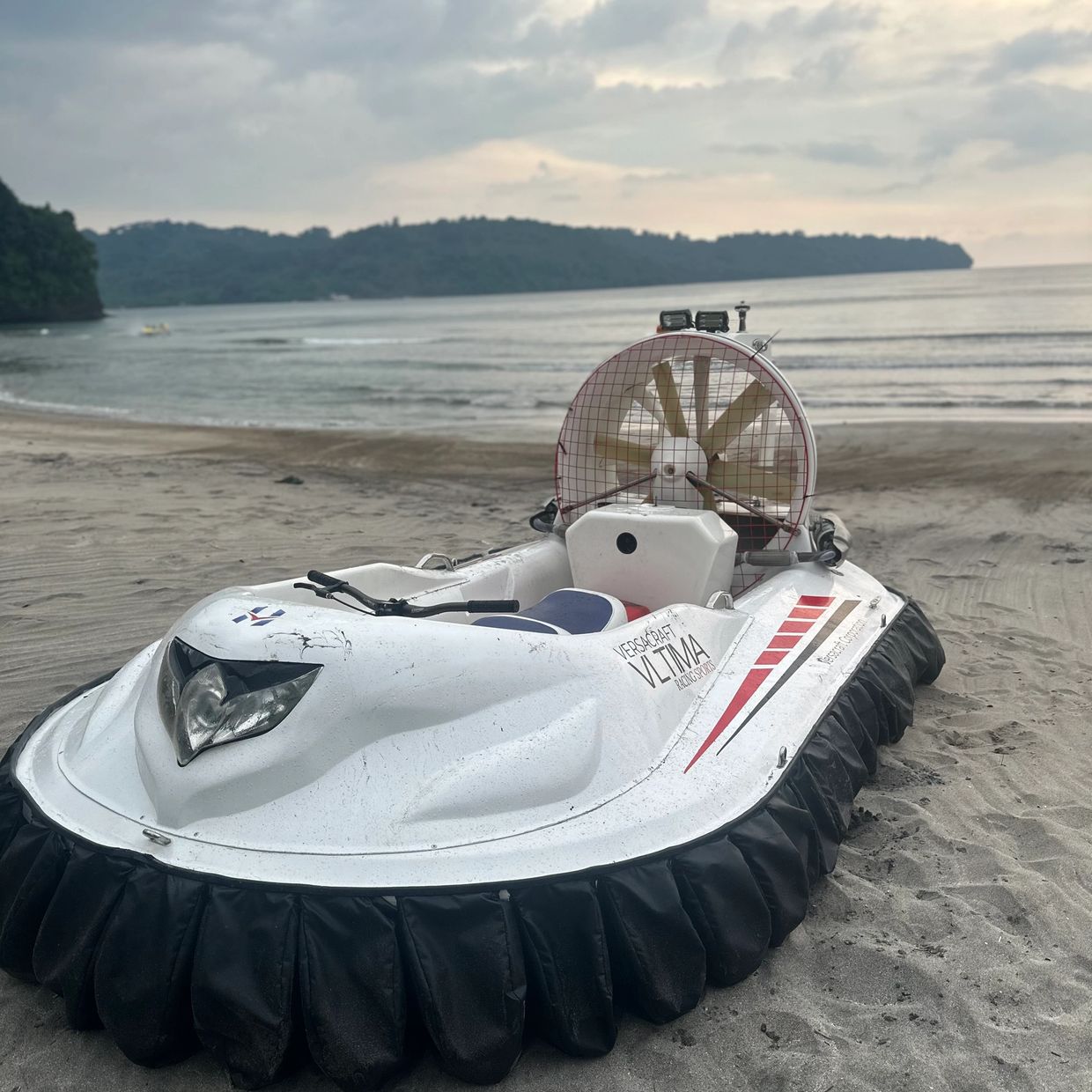White hovercraft on sandy beach with ocean and hills in background.
