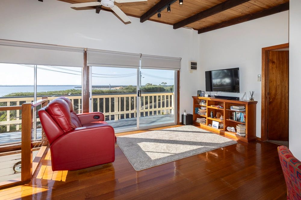 Bright living room with red leather recliner and ocean view through sliding glass doors.