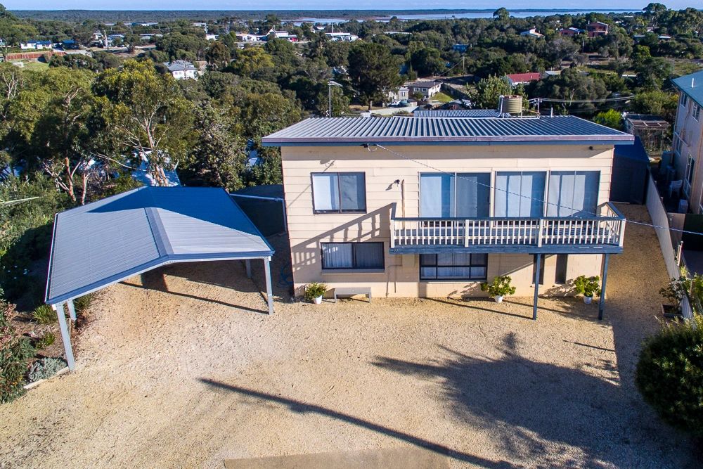 A beige two-story house with a balcony and a blue carport in a spacious yard.