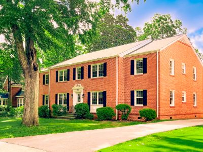 A two-story red brick house with black window shutters.