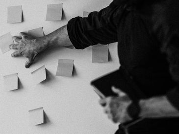 Person organizing sticky notes on a wall while holding a tablet.
